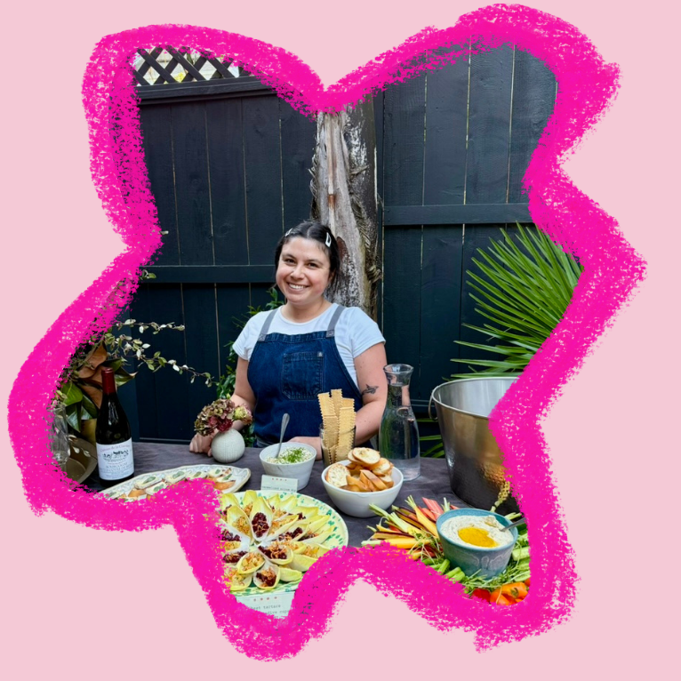 Tash smiling behind an outdoor table set with colorful platters and small bites